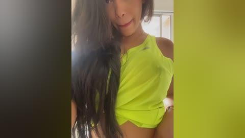 Video of a young woman with long, dark hair, wearing a lime green sports bra, standing in a bright room with green and yellow walls.