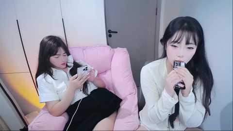 Video of an East Asian woman with long black hair, fair skin, and bangs, wearing a white blouse and black skirt, playing a white Nintendo Switch on a pink beanbag chair.