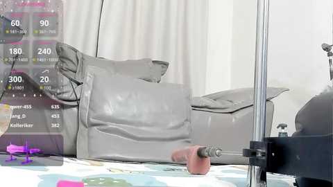 A video of a man's hand holding a gray, textured penis-shaped vibrator, positioned on a white, patterned blanket with a digital screen overlay displaying a game interface.