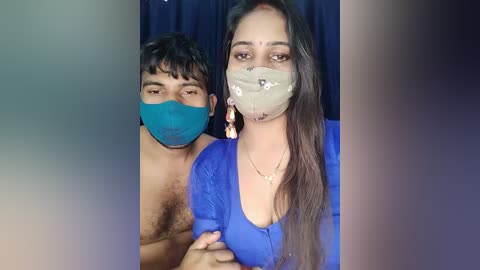 A video of two individuals with masks, one with a blue mask and a blue shirt, the other with a floral mask and a blue top.