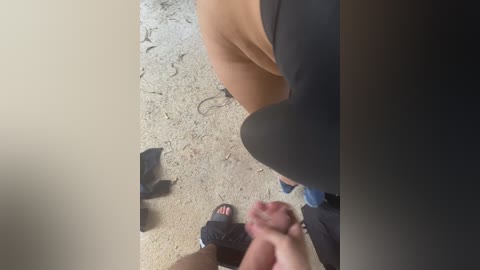 Video showing a person's legs in black shorts, a beige sandal, and black socks, standing on a beige carpet with scattered black cables.