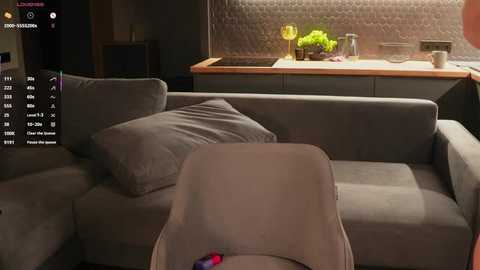 Video of a modern, dimly lit living room with a gray sectional sofa, wooden kitchen countertop, and a textured backsplash, featuring a virtual reality headset on the sofa.