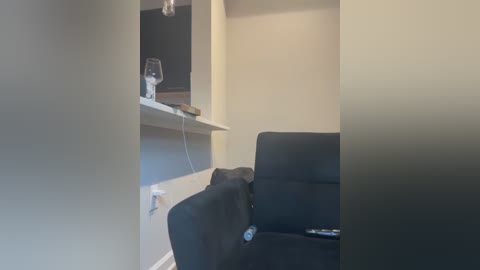 Video of a minimalist living room with a black sofa, a white shelf holding a glass and a remote, and a beige wall.