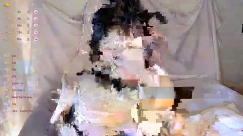 Video of a bed with a white sheet, partially obscured by pixelated distortion. The image has a glitchy, abstract appearance with an indistinct, possibly female figure beneath the sheet.