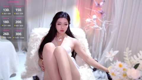 Video of a slim, fair-skinned Asian woman with long black hair, sitting cross-legged in a white, fluffy chair, wearing a white dress, surrounded by white flowers and sheer curtains in a soft, dreamy setting.