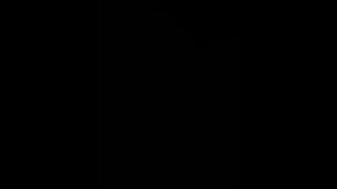 A black-and-white video of a lone figure standing in a dark room, illuminated only by a dim light source behind the subject, creating a stark contrast and a sense of mystery.