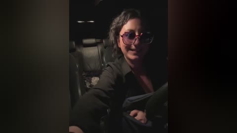 Media: Video of a middle-aged man with short, dark hair and glasses, smiling, wearing a black jacket, sitting in a dimly lit car.