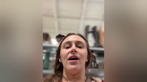 Media: Video of a woman with long brown hair, wearing a black top, smiling and laughing, with blurred background objects in a white room.