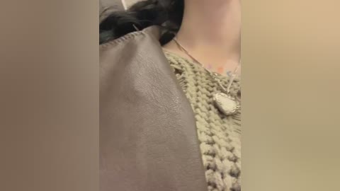 A close-up video of a woman's arm, showcasing a gray leather handbag and a chunky knit sweater with a heart pendant necklace.
