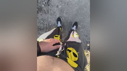 Video of a person wearing black shorts with yellow Batman logo and black sneakers, holding a black leash with a dog in the background.