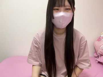 Video of a young Asian woman with long black hair, wearing a pink face mask, pink t-shirt, and sitting on a pink bed.