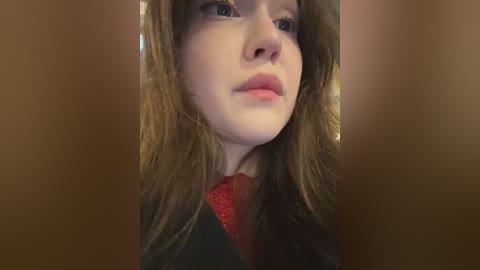 A close-up video of a young Caucasian woman with fair skin, brown hair, and blue eyes. She wears a red sweater, with a blurred background of a dark room.