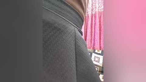 Video of a person wearing tight, textured gray leggings and a brown top. Background includes a pink curtain and framed pictures on a wall.