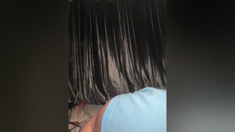 A video shows a person with shoulder-length, shiny black hair tied back with a black ribbon. They wear a light blue shirt, and the background is dimly lit.