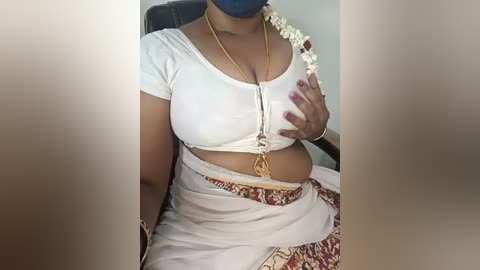 Video of a South Asian woman in traditional attire, white blouse and sari with floral patterns, wearing a blue face mask.