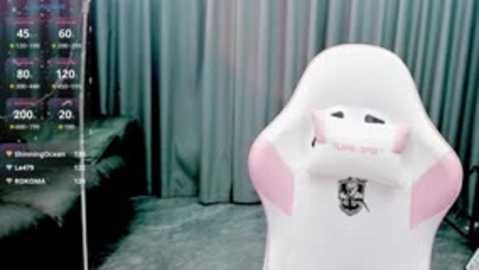 Video of a white, plush ghost-like chair with pink ears, positioned in front of a dark, curtained backdrop. A digital screen displaying gaming stats is visible to the left.
