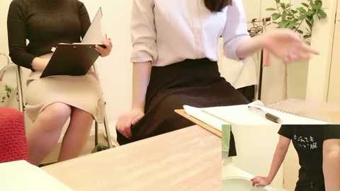 Video of a woman in a white blouse and black skirt, seated at a table with a man wearing a black T-shirt, both engaged in a drawing activity.