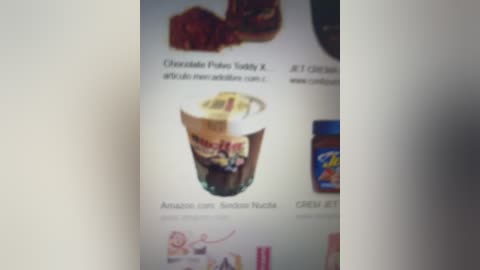 A blurred video showing a white background with a chocolate pudding container, \"Amazin' Chocolate Pudding,\" and a \"Cheese-It\" snack bag, both labeled. The image appears dimly lit.