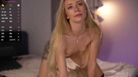A video of a nude, slim, blonde woman with small breasts, kneeling on a bed, in a dimly lit room with purple walls.