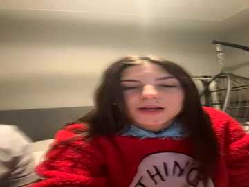 A video of a young woman with long brown hair, wearing a red \"THINK\" sweatshirt and blue shirt, eyes closed, mouth open, in a dimly lit bedroom.