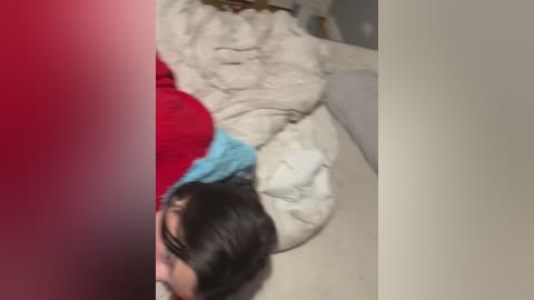 A blurry video shows a person with short dark hair wearing a red and blue jacket, lying on a beige couch with a white blanket.