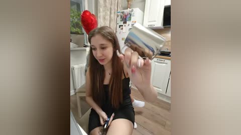 Video of a young woman with long brown hair, wearing a black dress, and a red heart hat, pouring cereal into a bowl in a modern kitchen.