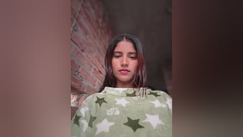 Video of a young woman with wet, dark hair, wearing a green towel with white stars, standing against a brick wall, creating a moody, introspective atmosphere.
