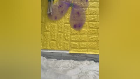 Video of a colorful, butterfly-shaped decoration hanging above a yellow wall with a textured pattern, and a white, fluffy carpet below.