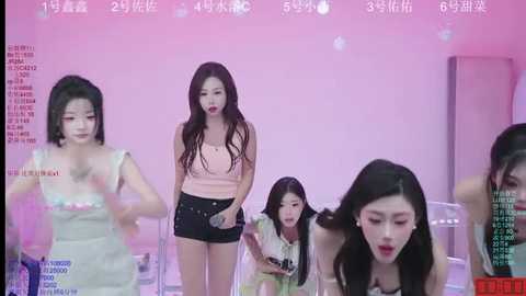 Video of four young Asian women in a bright pink room, one singing, one clapping, one reading, one sitting.