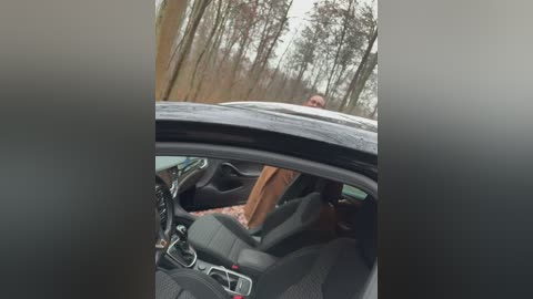 A blurry video shows a person with a brown jacket and a white dog inside a car, parked in a forest with bare trees.