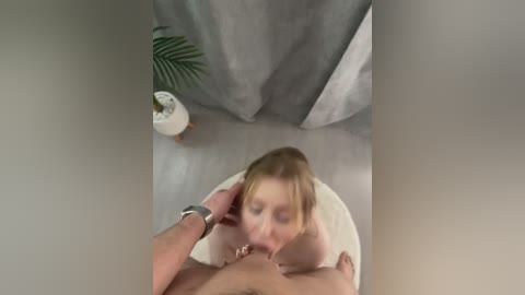 Video of a nude woman with fair skin and blonde hair performing oral sex on a man with a large erect penis in a minimalist room.