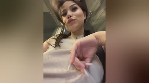 A video of a woman with fair skin, long dark hair, and wearing a white tank top, capturing a moment where she is removing a white glove.