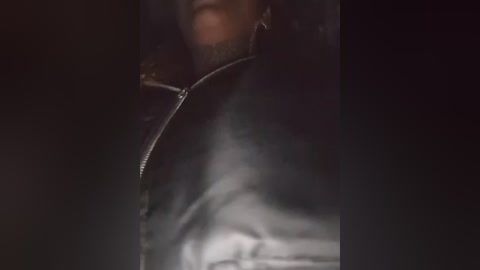 A close-up video of a man's upper body in a dark, dimly lit environment. He is wearing a black leather jacket and has a trimmed beard. The background is dark, with shadows creating a mysterious and slightly blurred atmosphere.