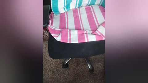 A video of a person's legs and chair, showing a black chair with a pink and white striped blanket draped over the backrest. The carpeted floor has a muted brown hue.