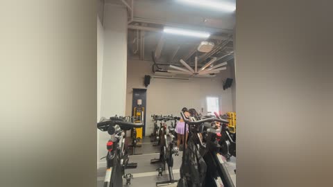 Video of a spacious, modern gym with rows of stationary bikes, a few people working out, and a high ceiling with exposed ductwork and fluorescent lights.
