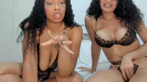 Video of two black women with curly hair, one with a large chest, in leopard print lingerie, kissing and smiling.