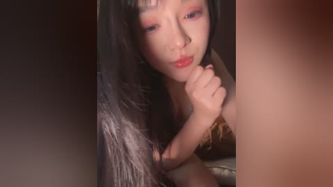A close-up video of an Asian woman with long, dark hair and light skin, wearing bold pink eyeshadow and a silver dress, her fingers lightly touching her lips.