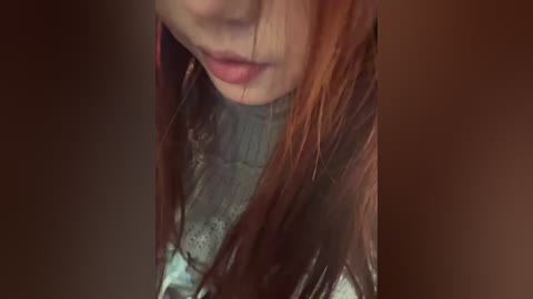 A close-up video of a woman with long, straight, reddish-brown hair, wearing a gray turtleneck sweater, focusing on her lips and chin.