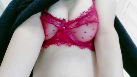 Video of a fair-skinned woman with medium-sized breasts wearing a sheer, red lace bra with polka dots, and a black shawl draped over her shoulders.