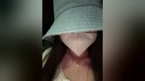 Video of a person wearing a light blue bucket hat and beige face mask, partially obscuring their face, with a gold necklace visible.