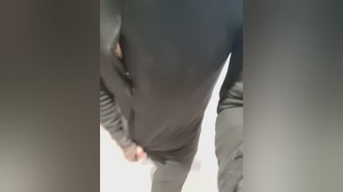 Video of a person's torso, wearing a black sweater and grey pants, captured from an overhead angle, blurry background, focusing on the body's midsection.