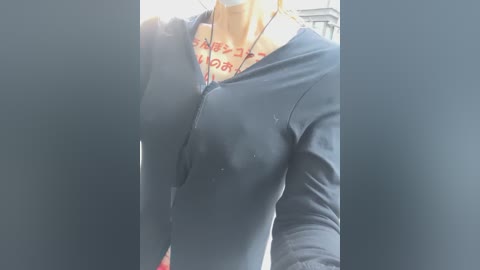 Video of a woman wearing a navy blue zip-up hoodie with a graphic tee underneath, partially revealing her breasts. The background is blurred, suggesting an urban setting.