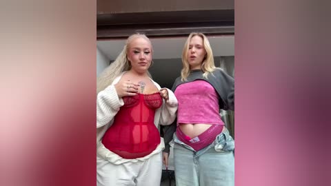 Video of two young women, one in a sheer red bra and white jacket, the other in a pink top and unbuttoned jeans, standing indoors with a blurred pink background.