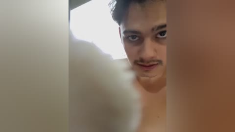 Video of a young, light-skinned man with short dark hair, looking intently through a frosted glass window, his expression serious.