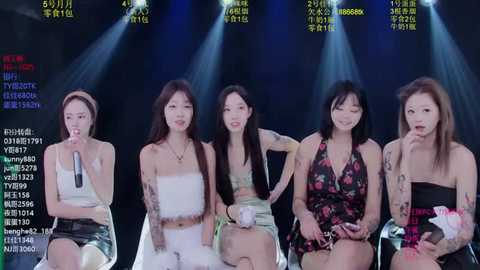 Video of five East Asian women in casual, floral dresses on stage, holding microphones, smiling, surrounded by bright stage lights and Chinese text.