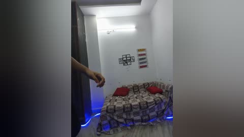 A video of a dimly lit, minimalist room with a white wall, a red couch, and a person's hand entering from the left.