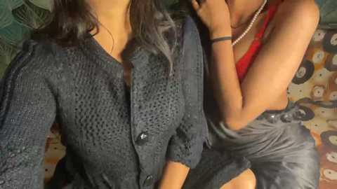 Video of two women: one in a dark, knitted sweater, the other in a red top, cuddling closely on a patterned couch.