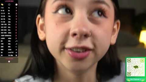 Video of a young Asian girl with dark hair, wearing a grey shirt, smiling widely. Background includes a blurred indoor setting. QR code and text overlay on the right.