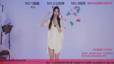 Video of an Asian woman with long black hair, wearing a white robe, singing into a microphone on stage. Background features Chinese text and colorful butterfly stickers.