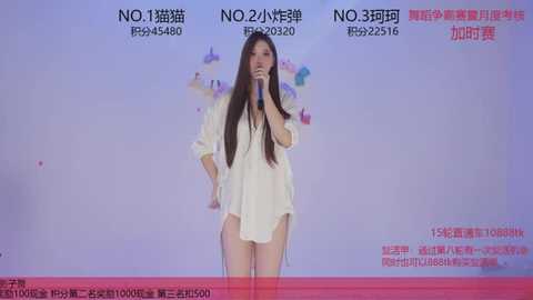 Video of a woman singing into a microphone, wearing a loose white shirt, on a stage with Chinese text on a blue and red background.